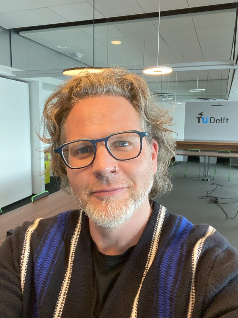 Portrait of scientific editor and science communication instructor, Michael Glennon, smiling with kind confidence while standing in a classroom.